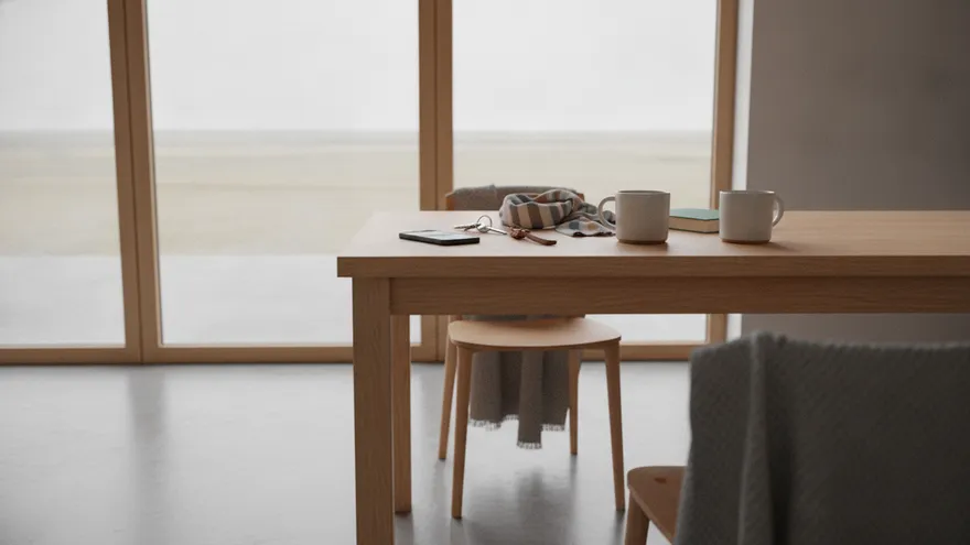 A table by a window in bright daylight with a phone, a set of keys, two mugs and a folded scarf left on it, and a grey throw over the chair beside it.
