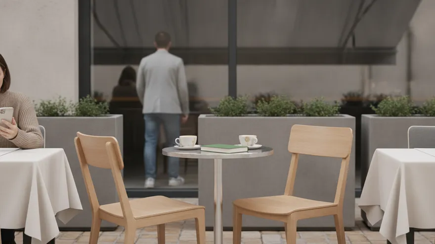 An outdoor café table with two cups left on it, empty chairs around it and someone walking away behind the glass.